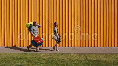 年轻漂亮的女人购物后快乐地散步。 年轻的男人跟着她，<strong>挣扎</strong>着拿着她的包。